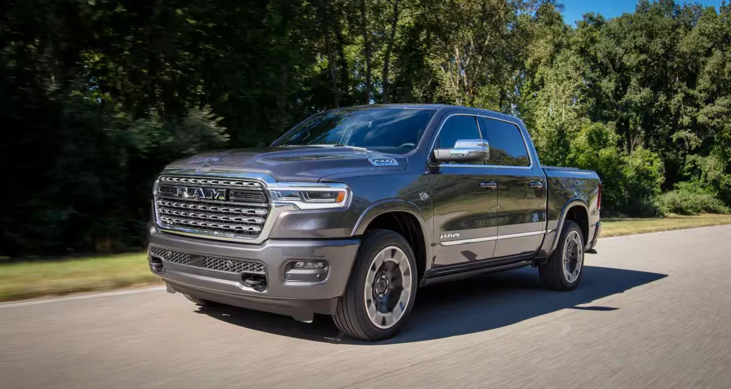 Gray 2027 Ram 1500 crew cab pickup driving on a paved road with trees and grass along the roadside