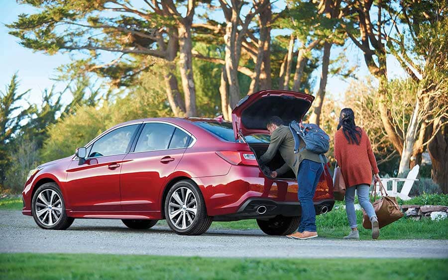 Couple loading the trunk of a red Subaru Legacy at a park