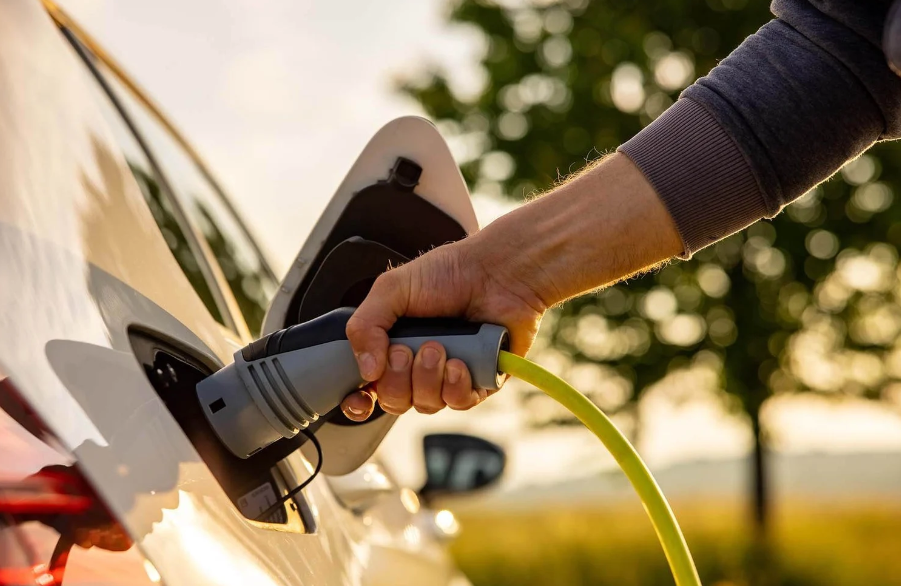 man plugs a charging cord into his electric vehicle; image only shows man's hand and charger going into the port