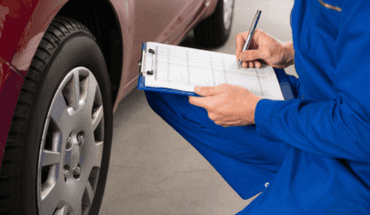 Technician with a clipboard inspecting a vehicle wheel and tire