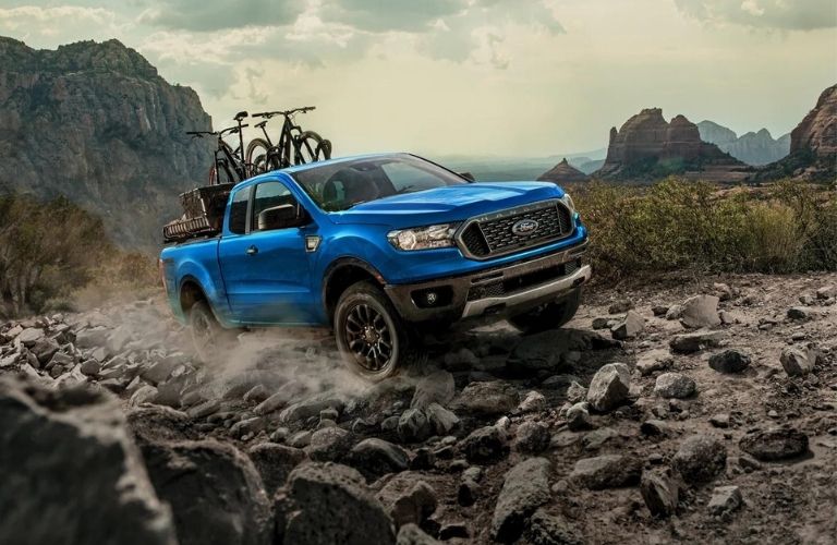 A blue 2022 Ford Ranger carrying cycles on a rocky terrain.