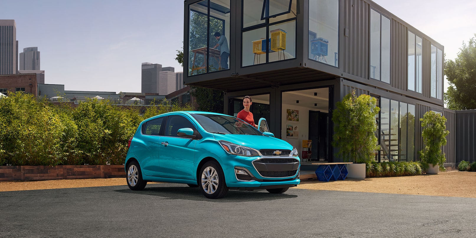 A woman stepping inside a blue 2021 Chevrolet Spark parked outside of her home