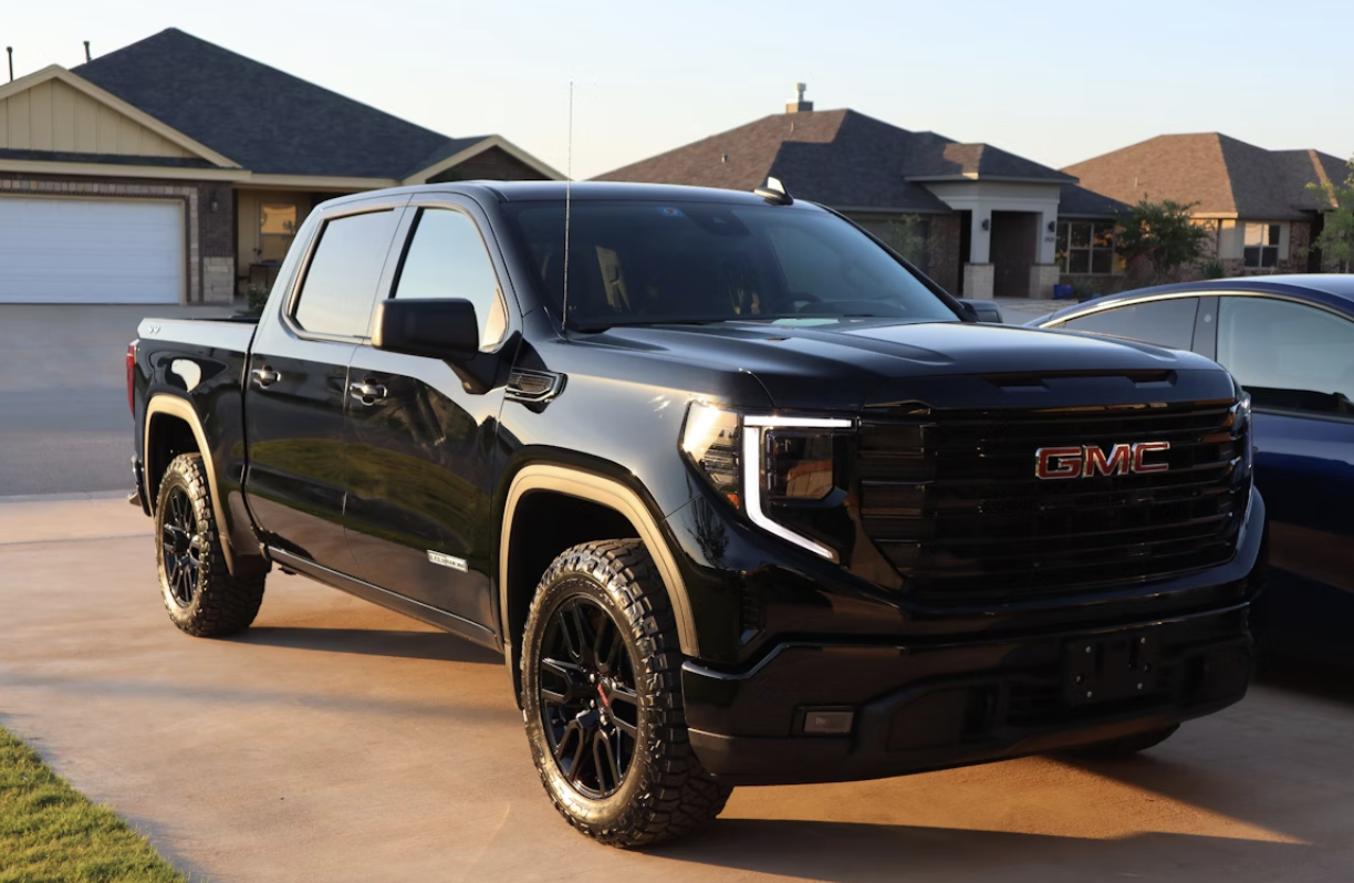 Black GMC pickup truck parked in a driveway at sunset, with a suburban home in the background.