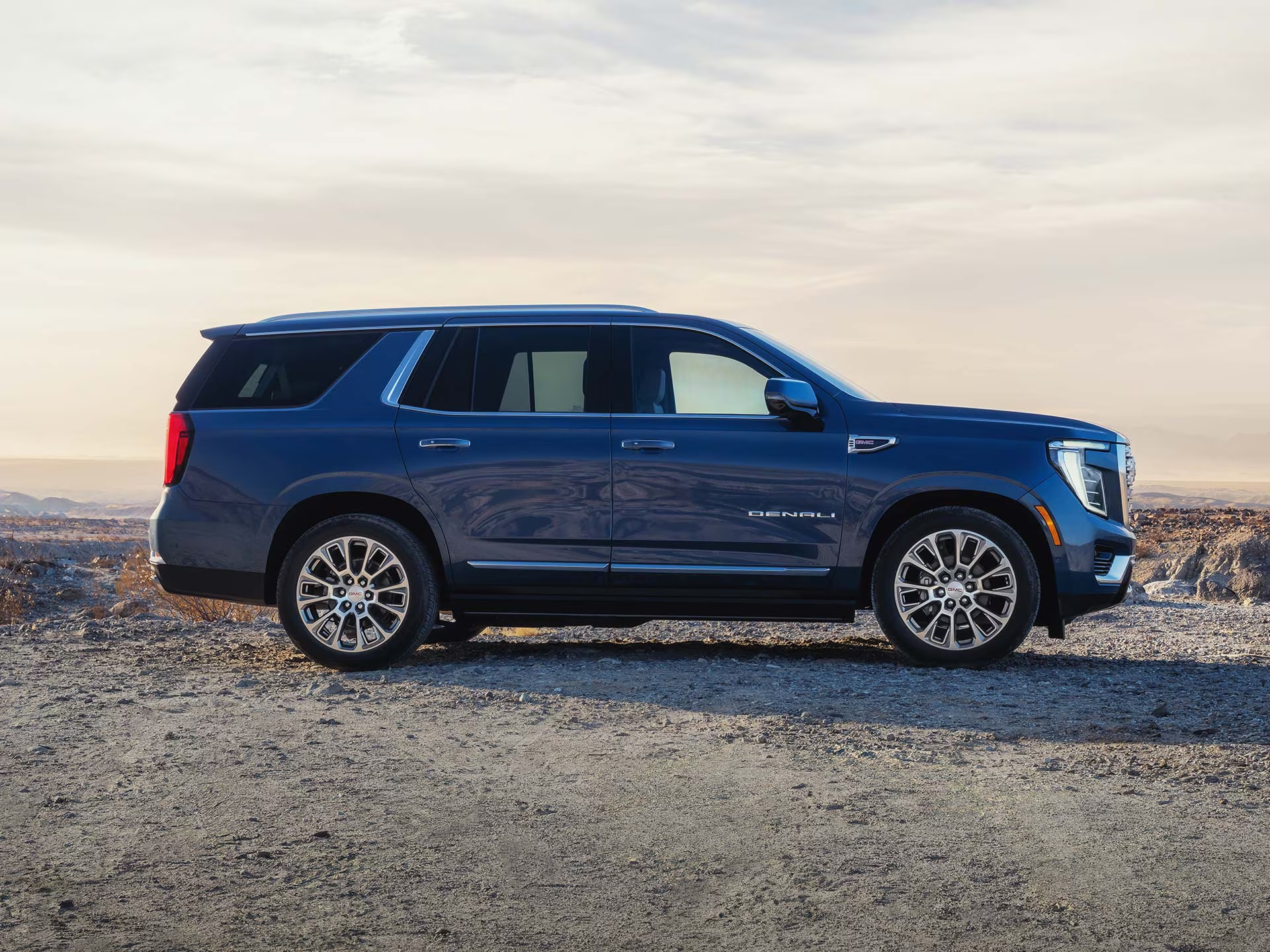 Blue GMC Yukon Denali parked on a gravel overlook at sunset