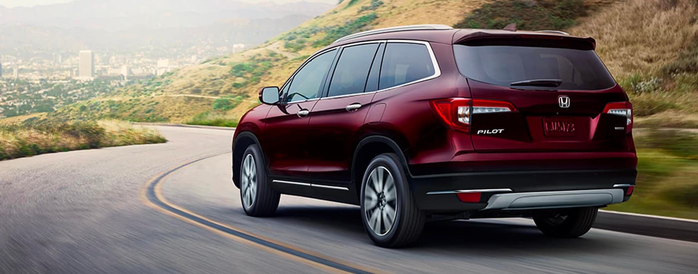 Maroon 2021 Honda Pilot Touring is driving down hill on a winding road