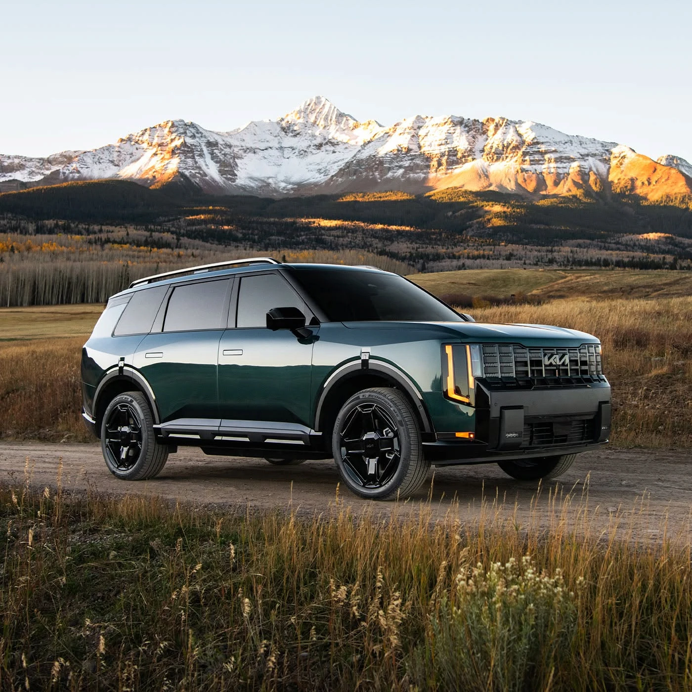 Dark green Kia Telluride parked on a dirt road with snow-capped mountains in the background at sunset