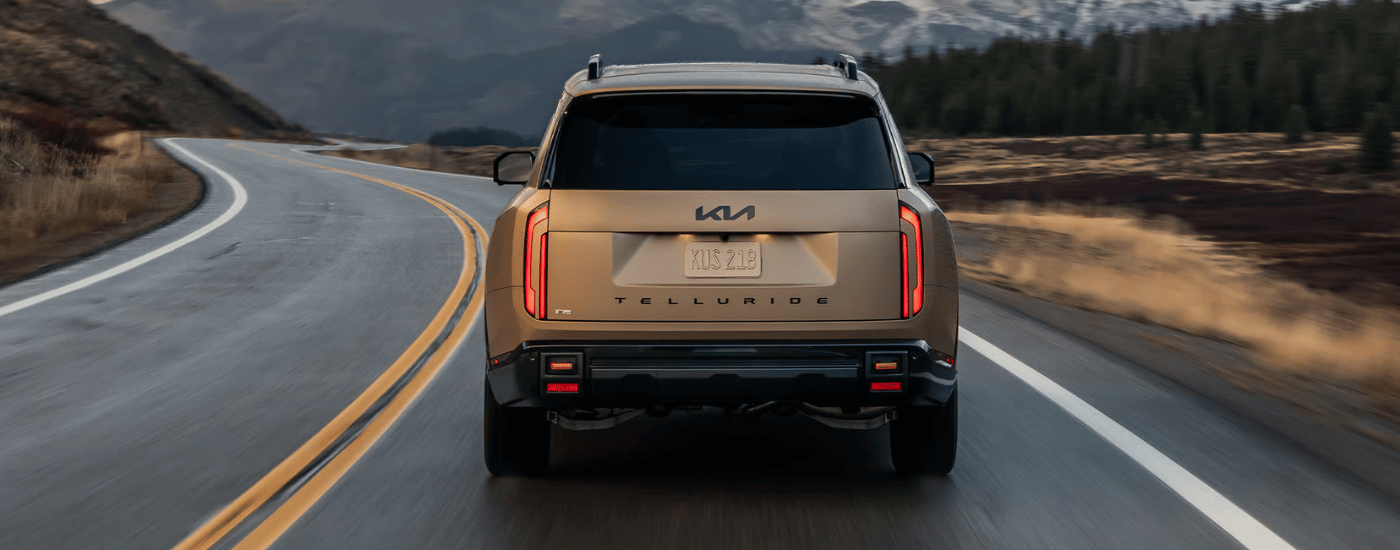 Rear of a brown 2027 Kia Telluride friving down an open winding road