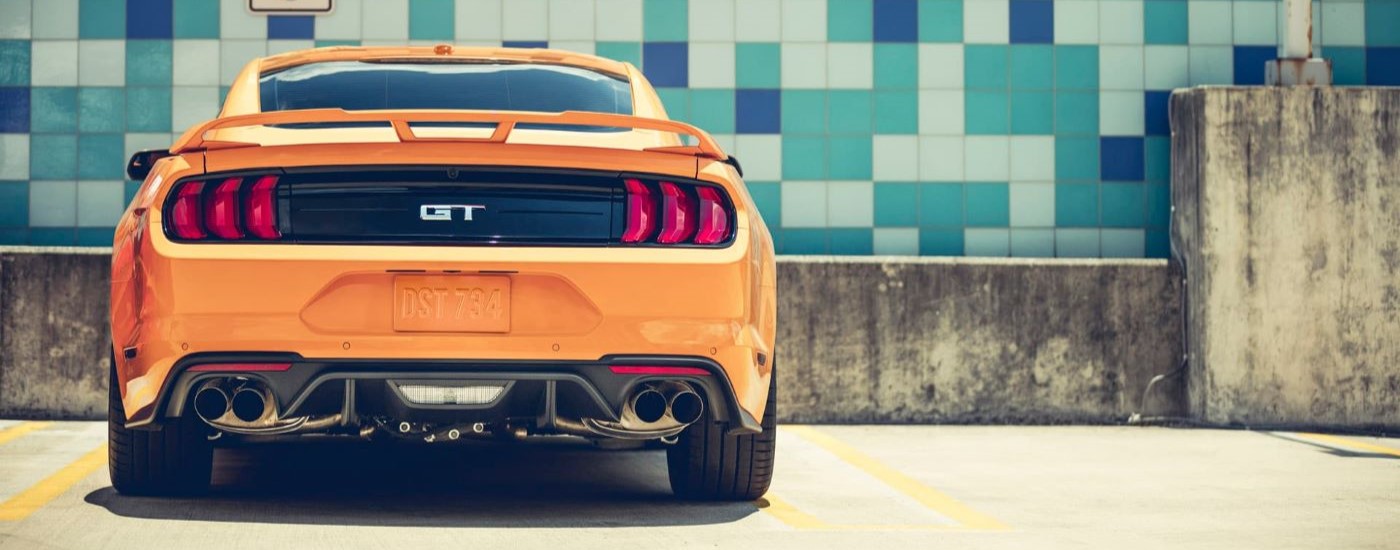 An orange 2018 Ford Mustang GT is shown from the rear near a tile wall.