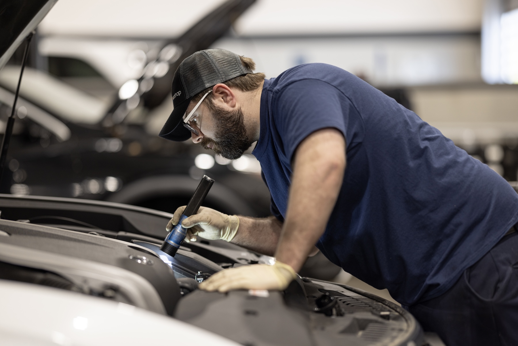 Service technician examining hood of car with flashlight. 