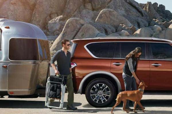 Couple with a dog beside a copper Nissan Armada towing an Airstream travel trailer