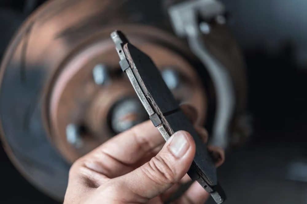 Hand holding a new brake pad next to a brake rotor