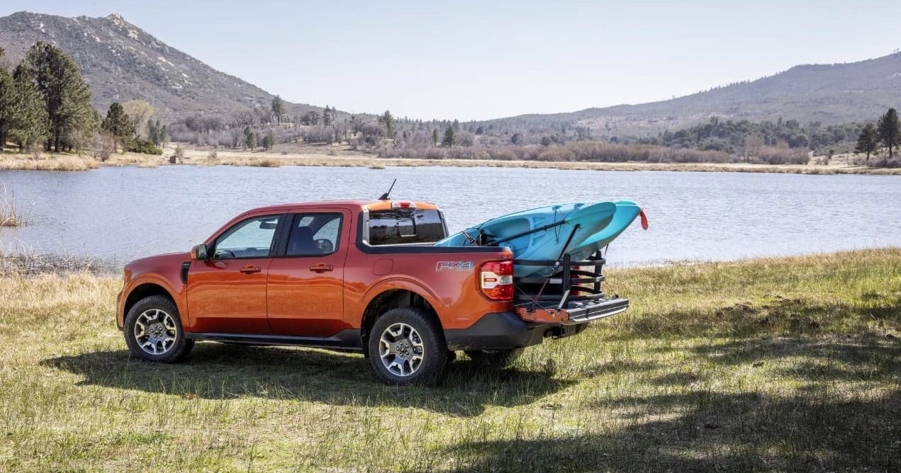 orange 2024 Ford Maverick parked by a lake with kayaks in the truck bed