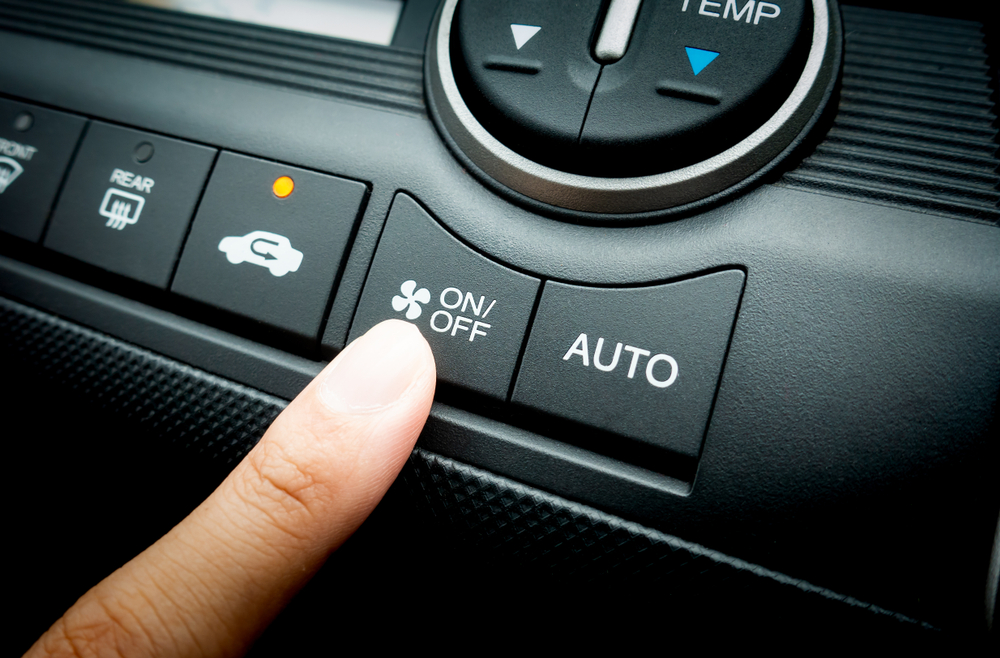 Finger pressing the fan button on a car's air conditioning control panel.