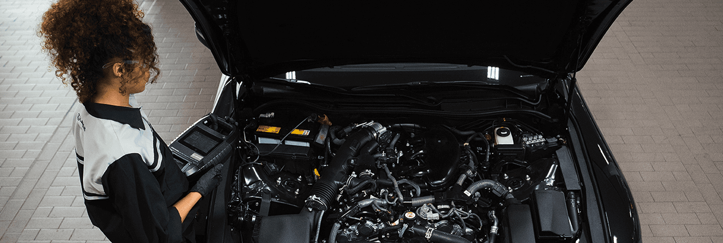 A Lexus service technician working underneath the hood of a vehicle