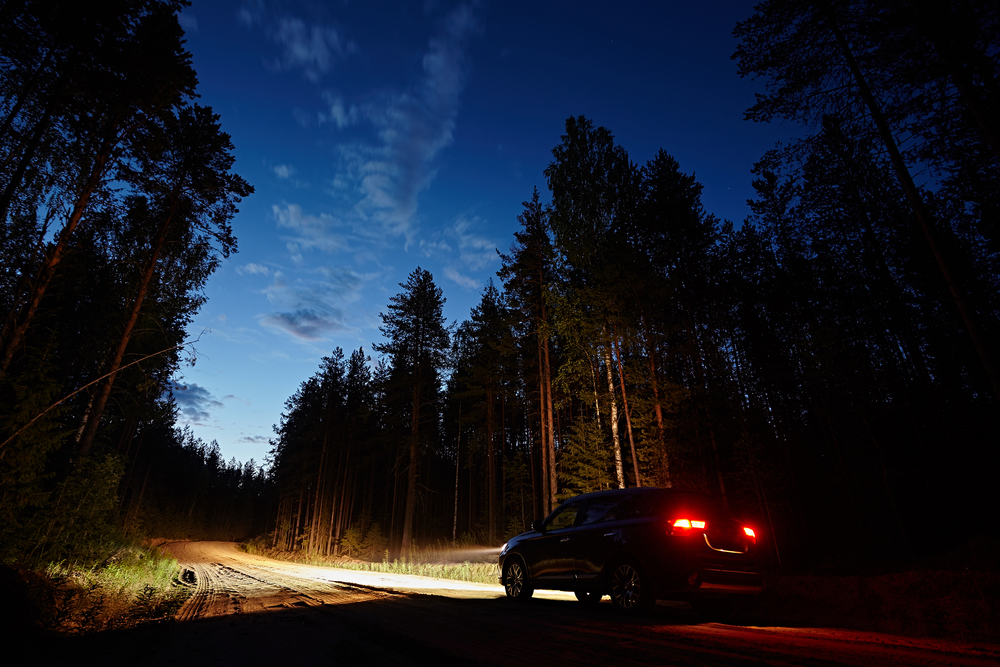 SUV driving down a dirt road at night with headlights and taillights on.