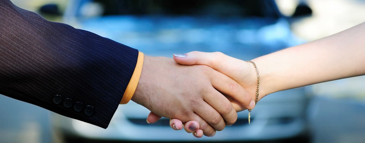 A salesman and customer are shaking hands at a dealership.