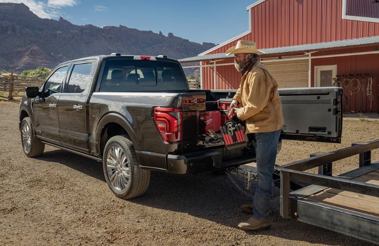 Man Loading Cargo in Bed of Black 2024 Ford F-150 with Pro Access Tailgate Open