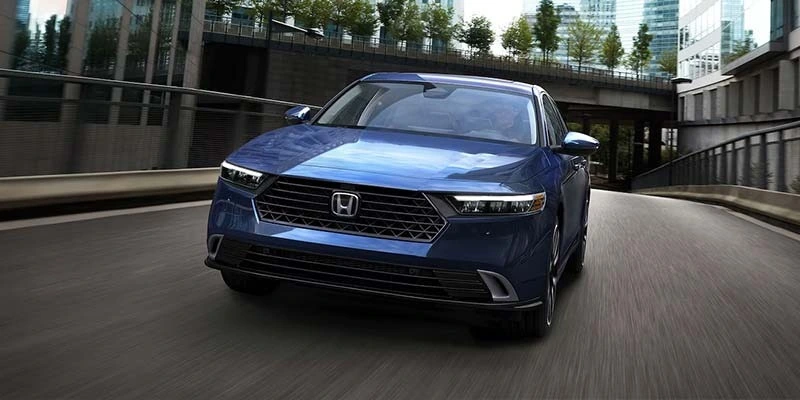 A blue Honda Accord driving through a modern city landscape