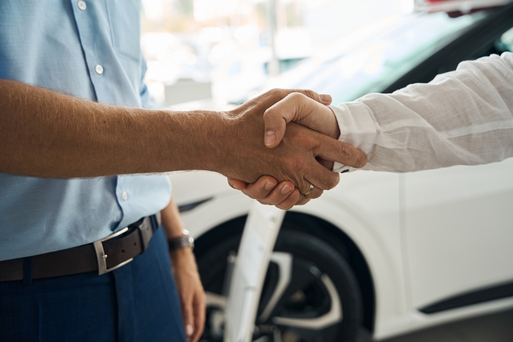 Salesman shaking hands with client in modern car dealership