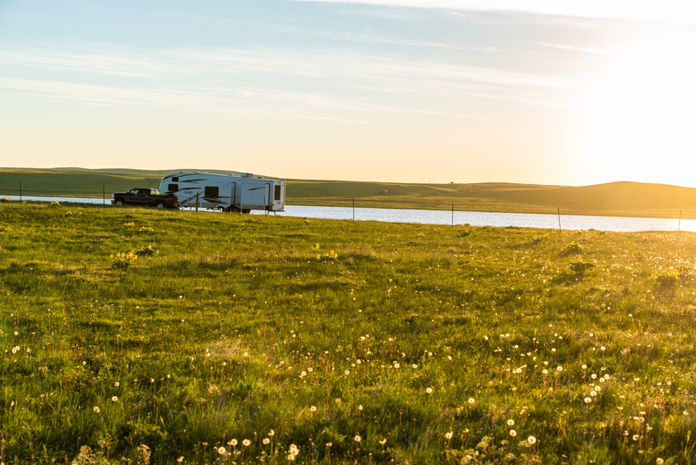 pickup truck towing a fifth wheel camper on a back road in the countryside while the sun sets