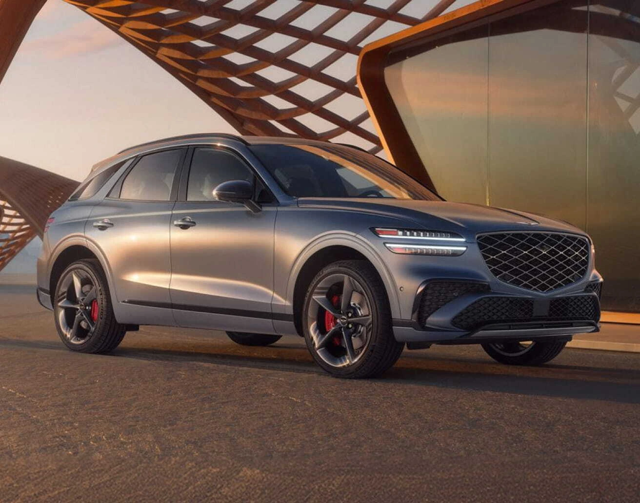 Gray Genesis SUV shown from a front three-quarter angle against modern architecture in warm sunset lighting.