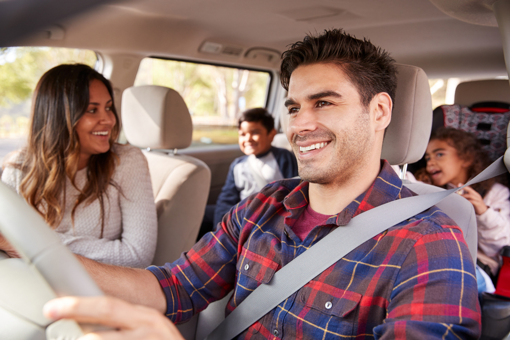 Father driving a car as wife looks at their two kids in the back seat