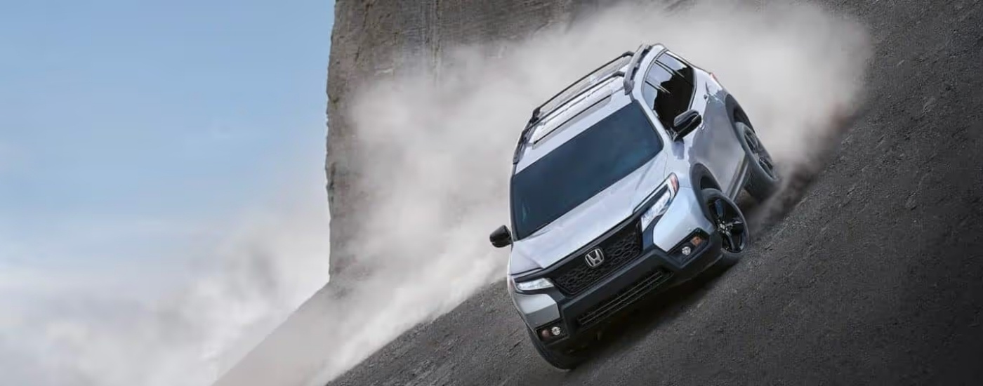 Silver 2021 Honda Passport Elite driving on a steep hill kicking up dust
