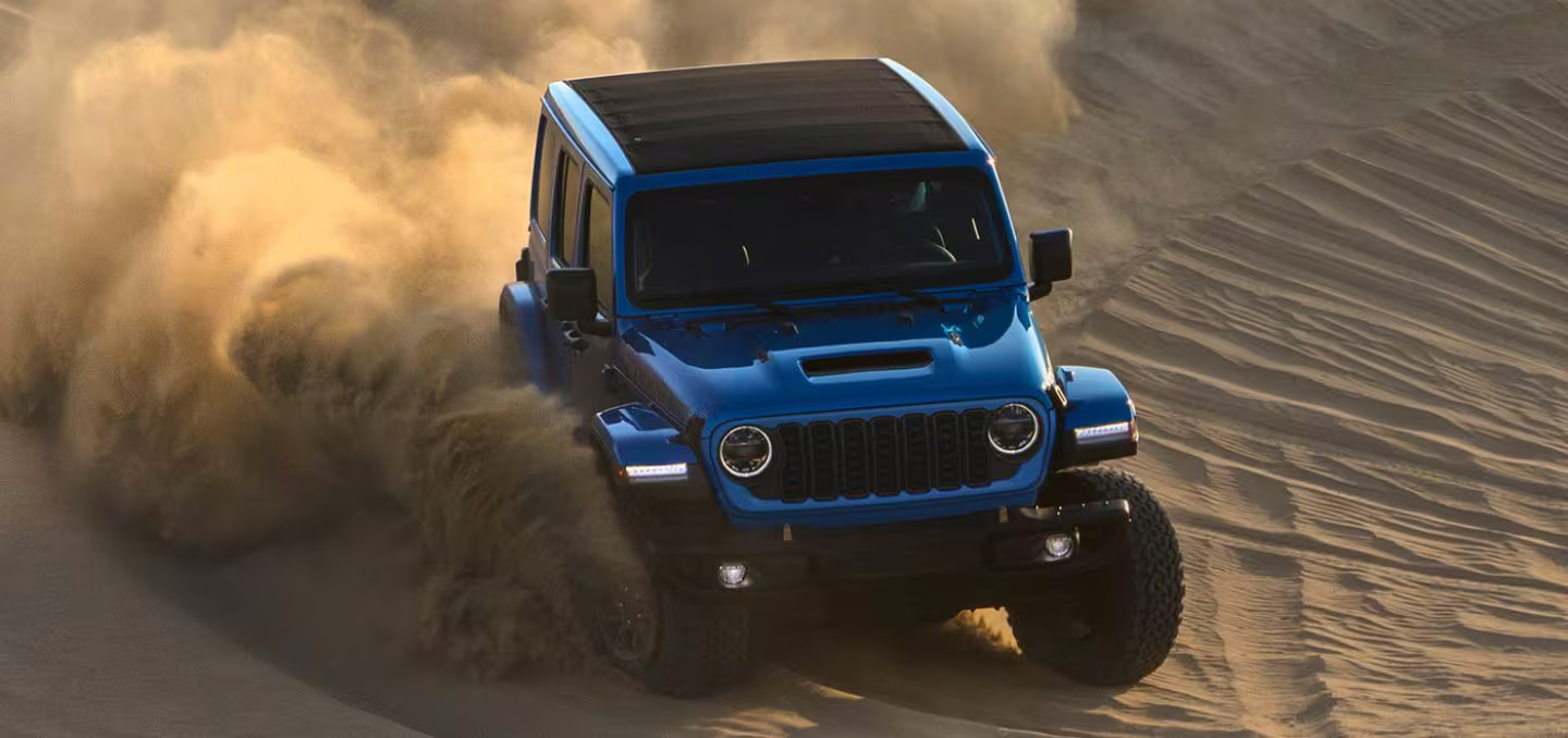 A blue jeep driving through the sand.