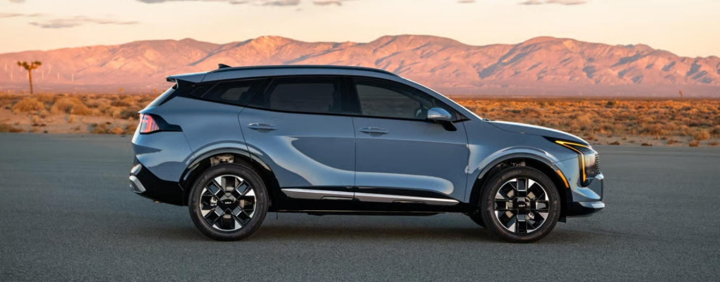 A blue 2026 Kia Sportage shown parked in front of mountains.