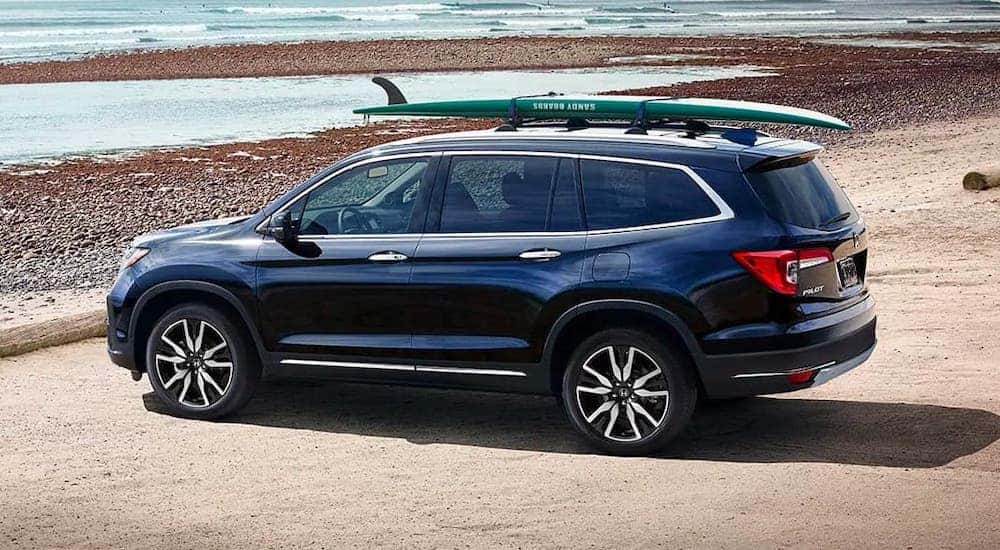 A blue 2020 Honda Pilot Elite is parked at a beach near Rochester with a surfboard on the roof.