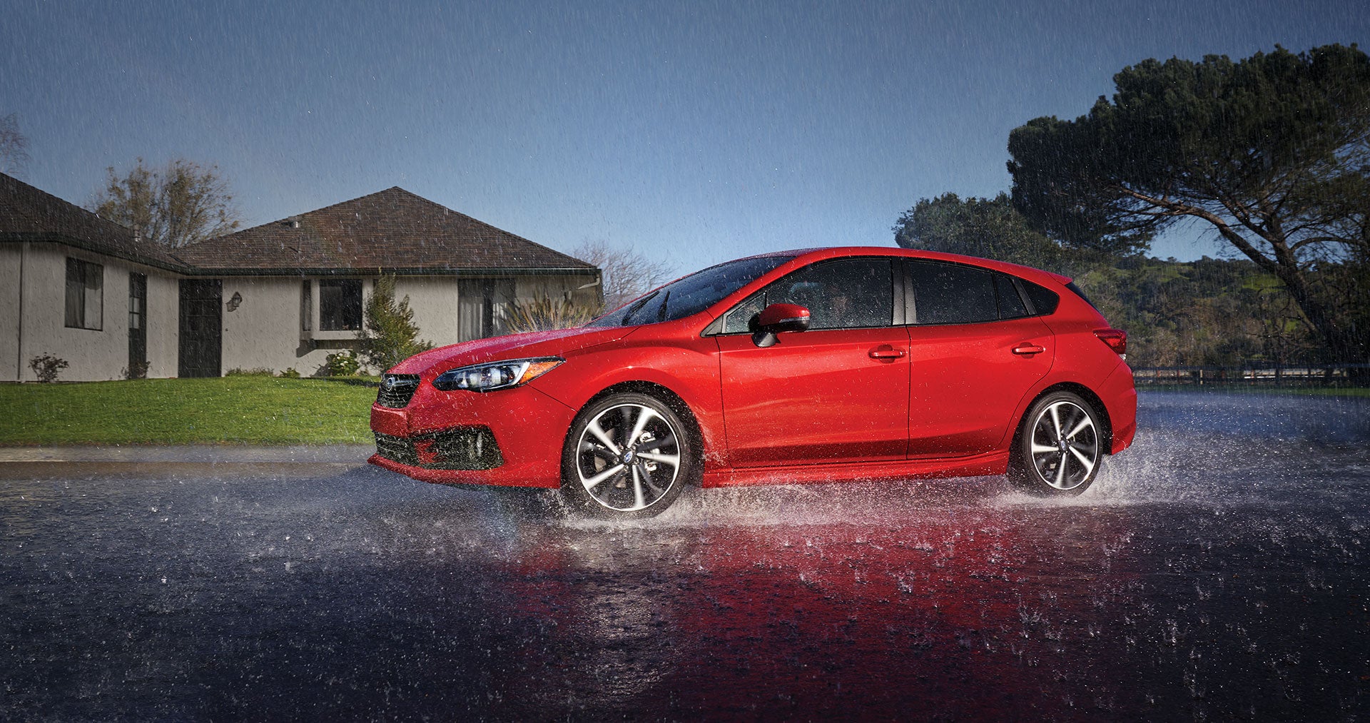 Red 2023 Subaru Impreza hatchback driving on a wet road