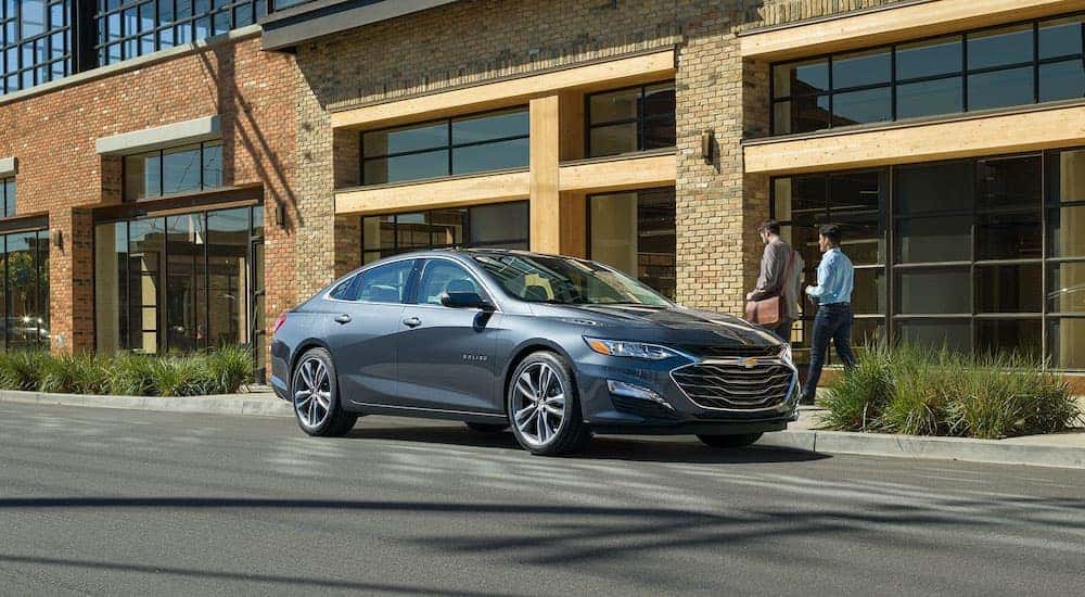 A grey 2020 Chevy Malibu is parked in front of a brick building.