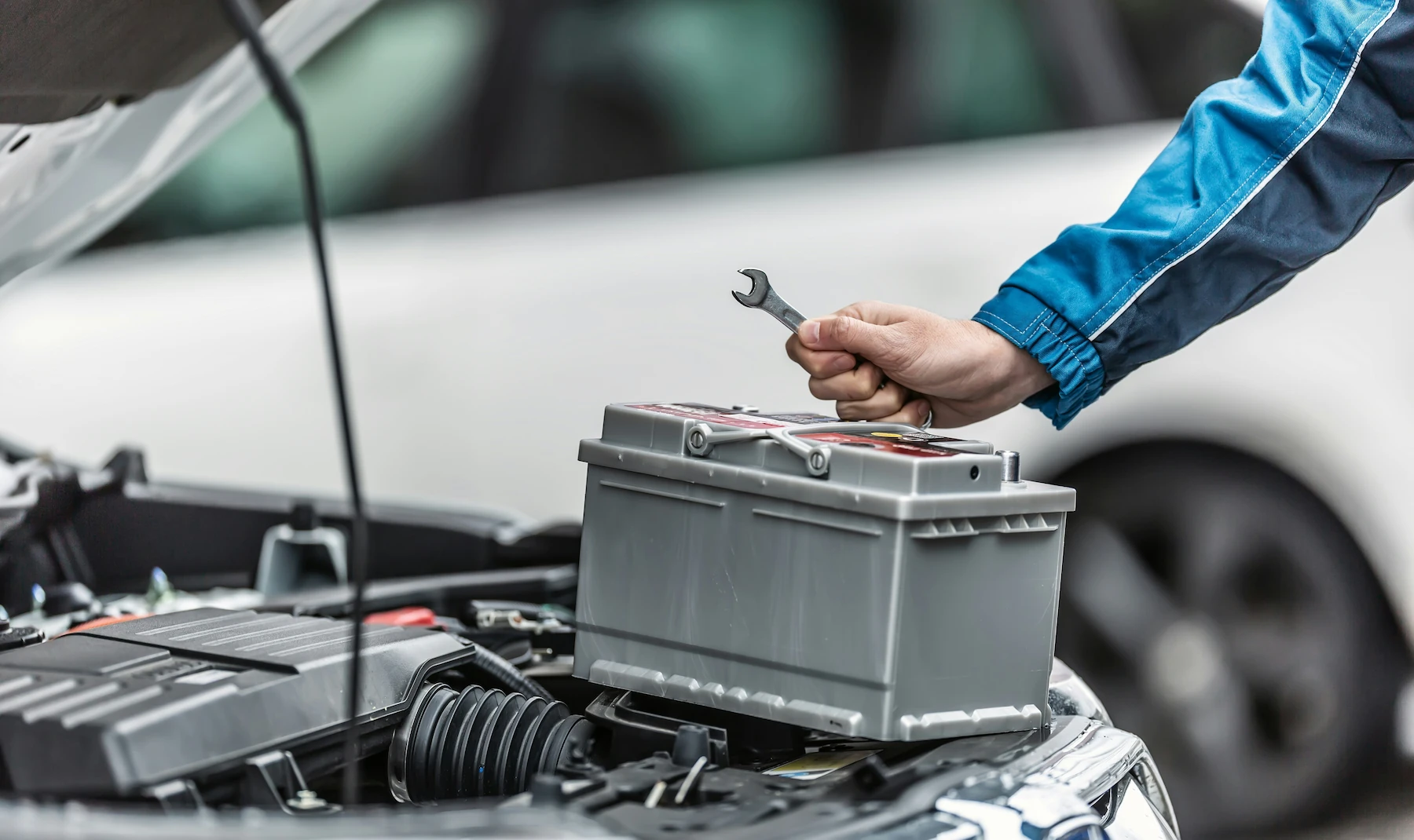 Technician's hand holding a wrench above a car battery while installing it in an open engine bay.