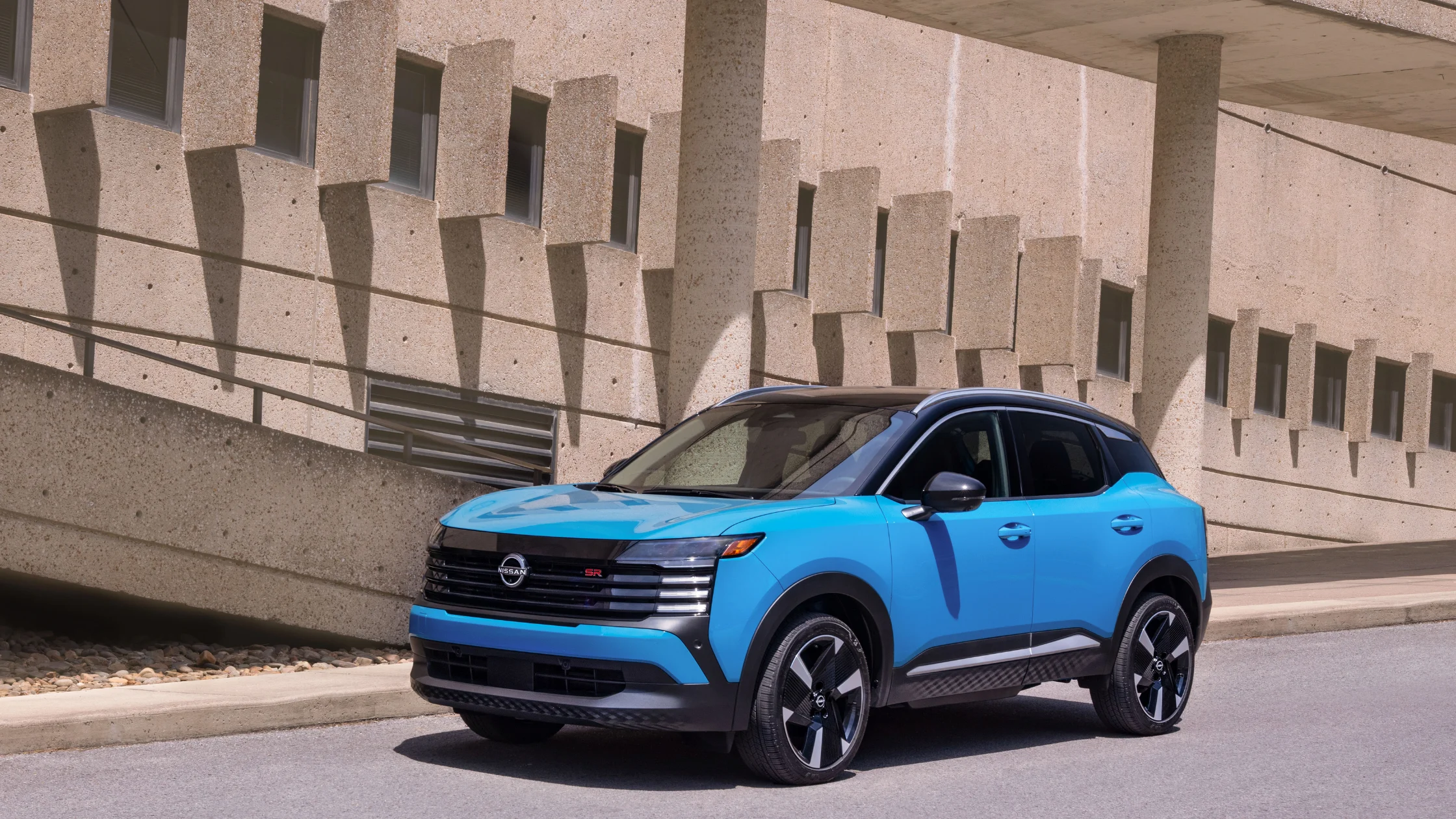 2026 Nissan Kicks® blue compact SUV parked by modern concrete building with black roof