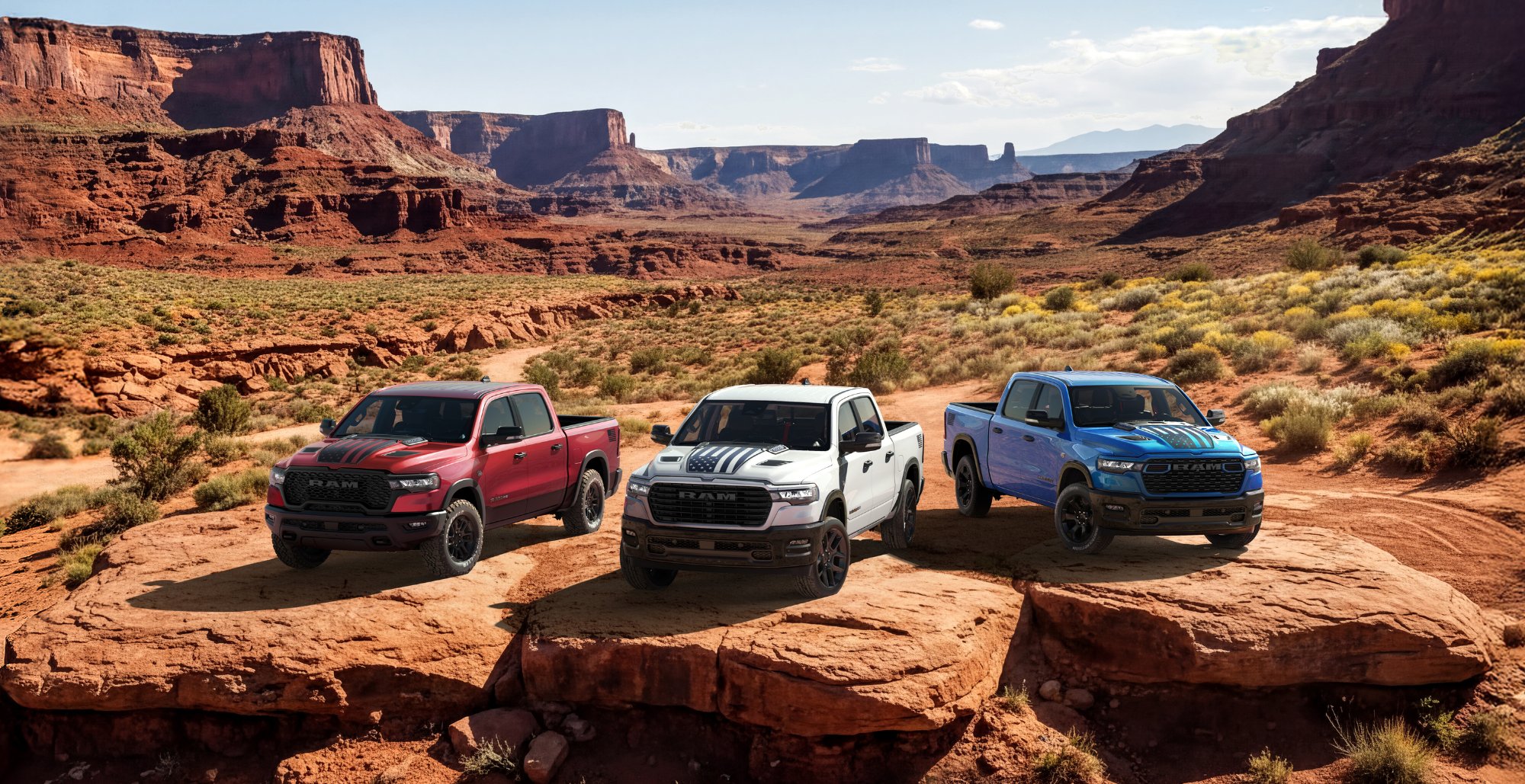 Three 2026 Ram 1500 pickups parked on red rock under a clear desert sky
