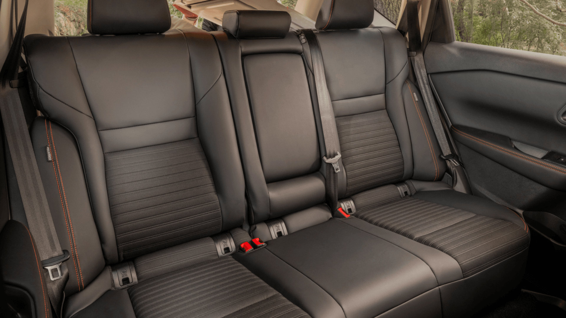2026 Nissan Rogue® rear cabin showing black seats, center armrest, seat belts, and orange contrast stitching.