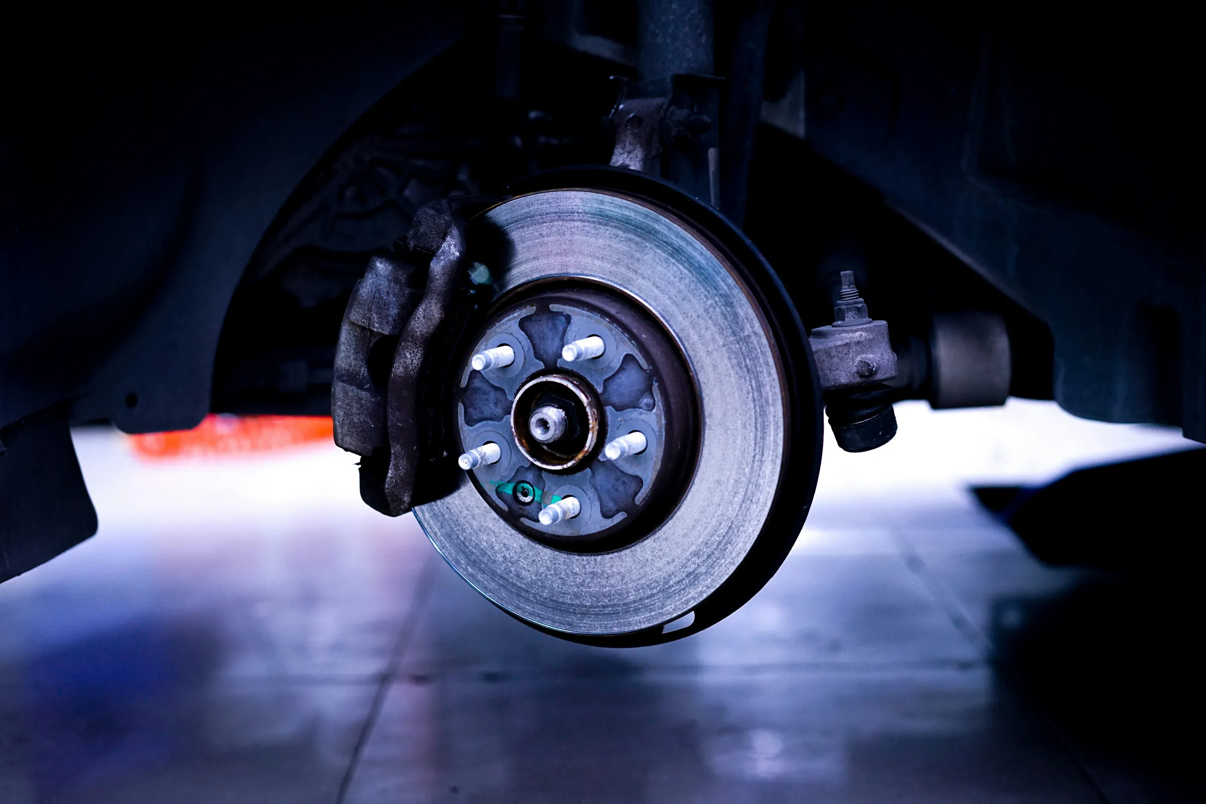 Close-up of a vehicle's brake rotor and caliper lit in blue, viewed from underneath the car. Brake Rotor Service in Kansas City, KS