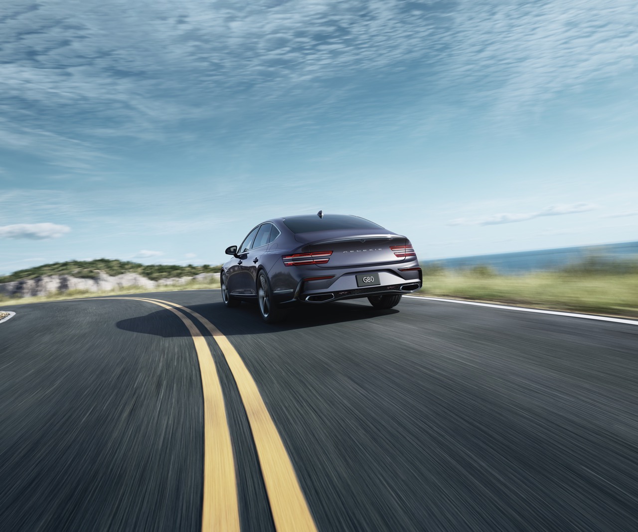 3/4 rear driver side view of Genesis G80 in Ceres Blue in motion driving on coastal road