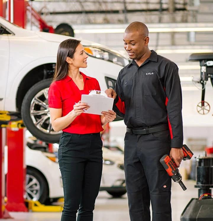 Kia service advisor and technician reviewing a vehicle checklist together, representing the prepaid maintenance covered by the Kia Care Service Plan