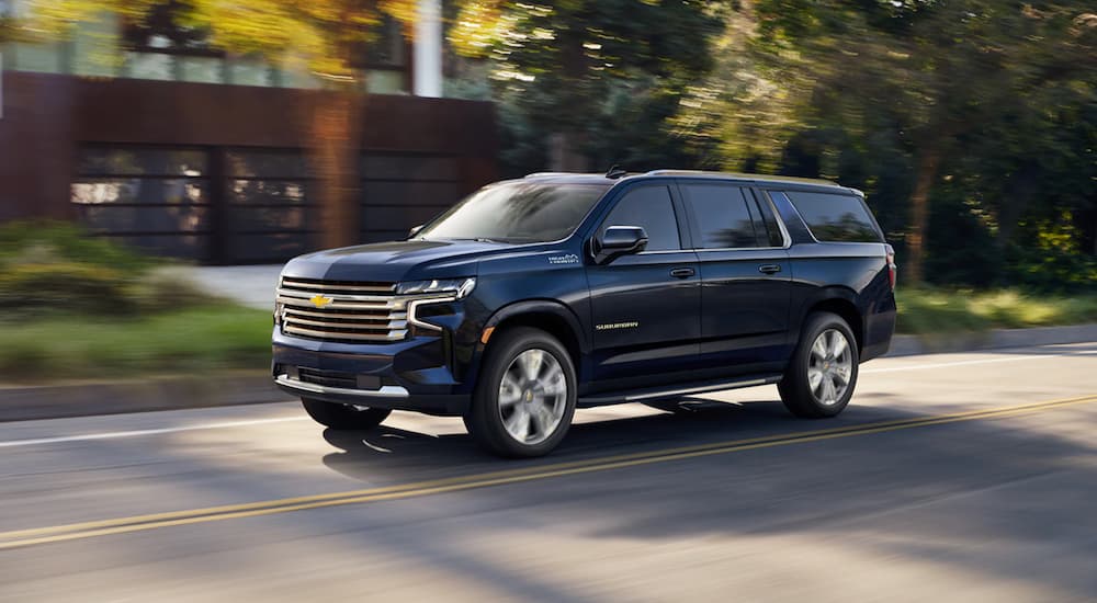 Dark blue 2021 Chevy Suburban High Country, a popular used SUV for sale, driving on a tree-lined road