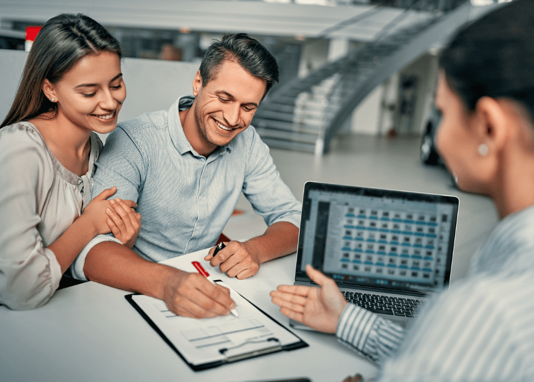 Couple discussing leasing options at Kiefer Kia dealership, with a focus on electric vehicles, reviewing documents and laptop screen displaying vehicle images.