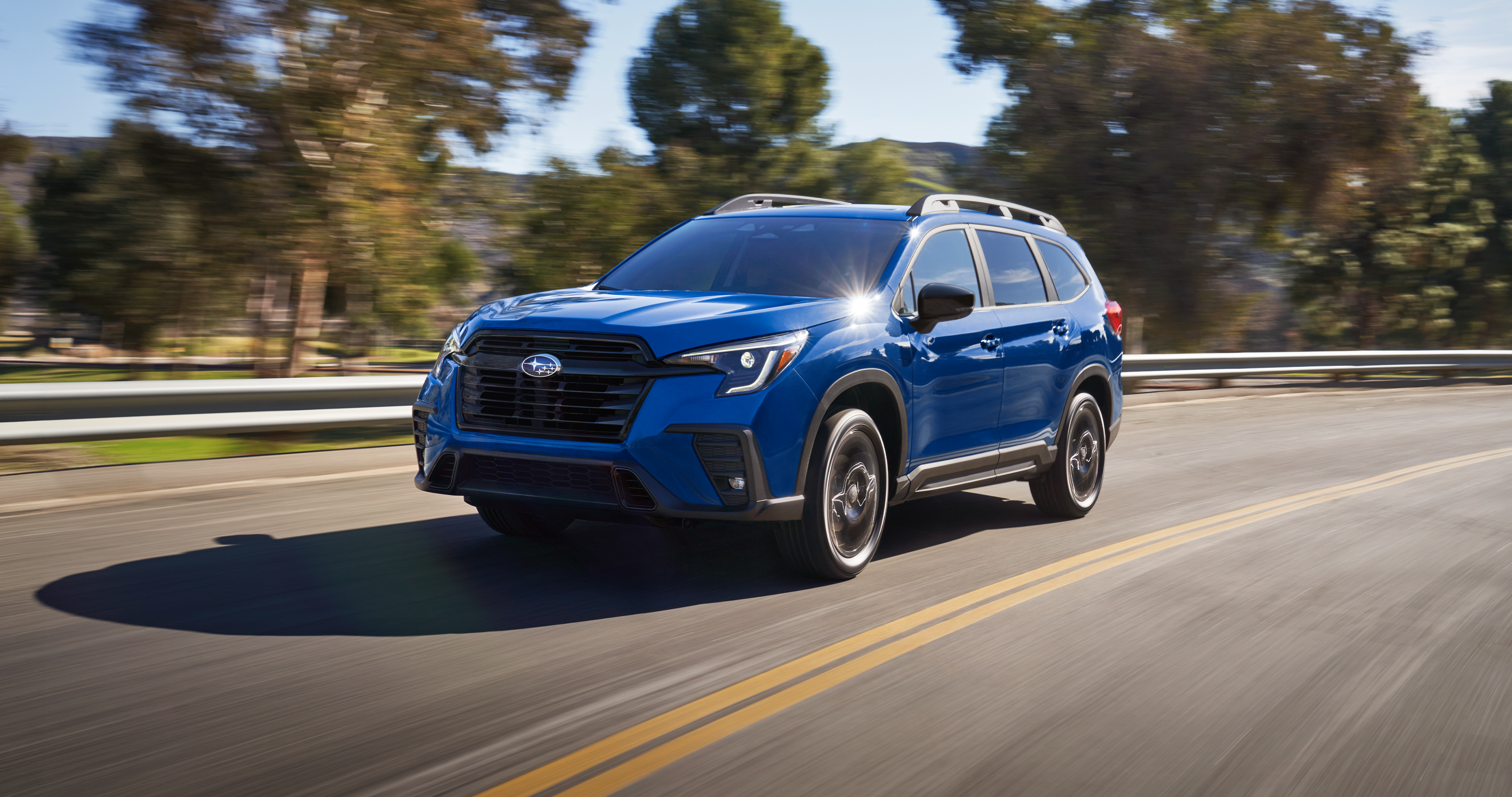 A blue Ascent 3-row SUV drives on a rural highway. 