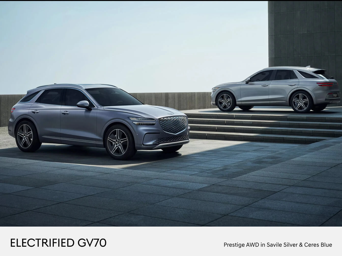 Two 2026 Genesis Electrified GV70 Prestige AWD models, one in Savile Silver and one in Ceres Blue.