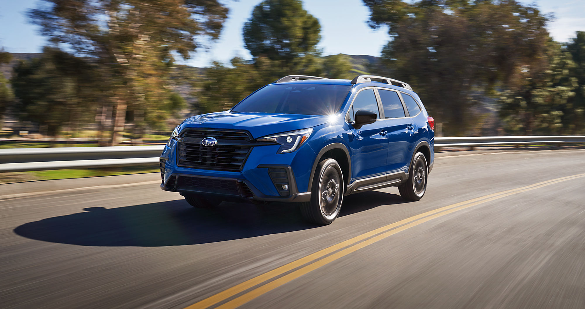 2027 Subaru Ascent three-row SUV in blue driving along a country road