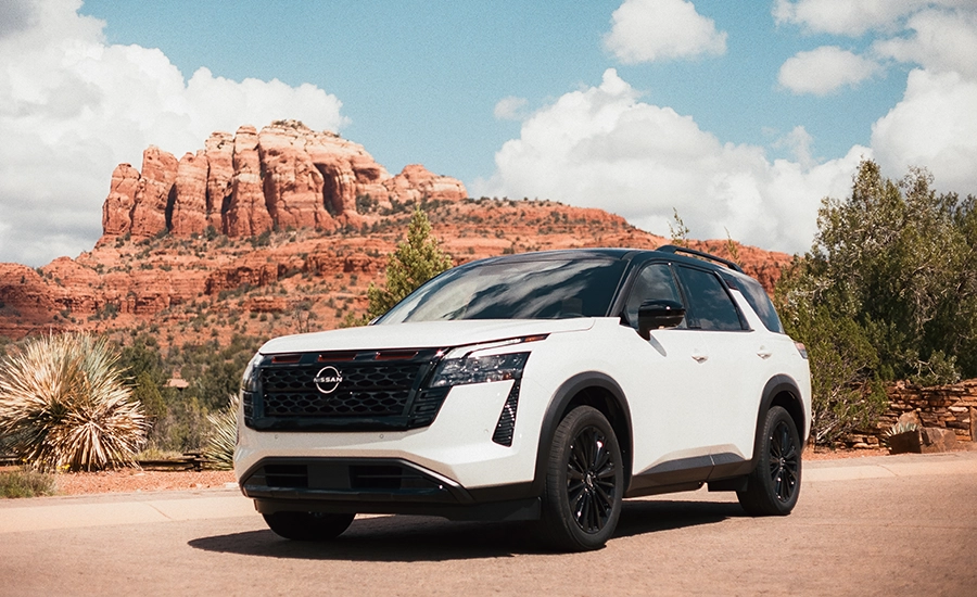 White 2027 Nissan Pathfinder SUV with black wheels photographed in a desert landscape with red rock formations.