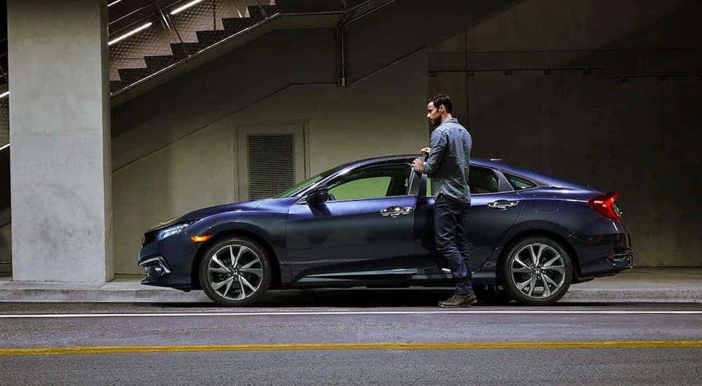 A man is about to get into a blue 2021 Honda Civic Sport that is parked under a bridge in Rochester, NY.
