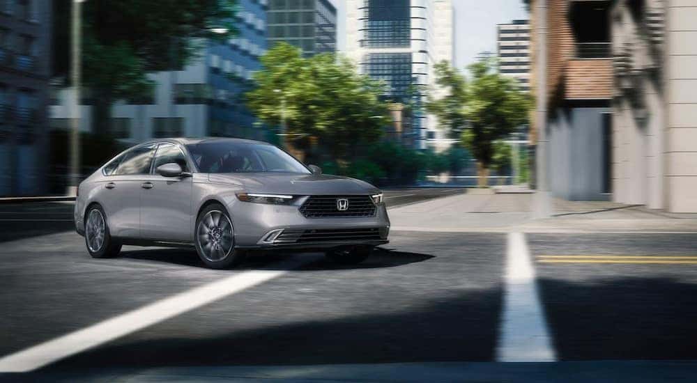A gray 2024 Honda Accord EX-L Hybrid is shown driving on a city street.