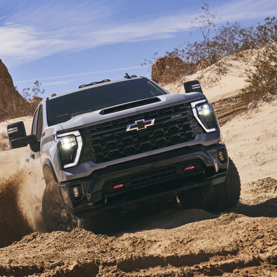 A gray truck driving through the sand.