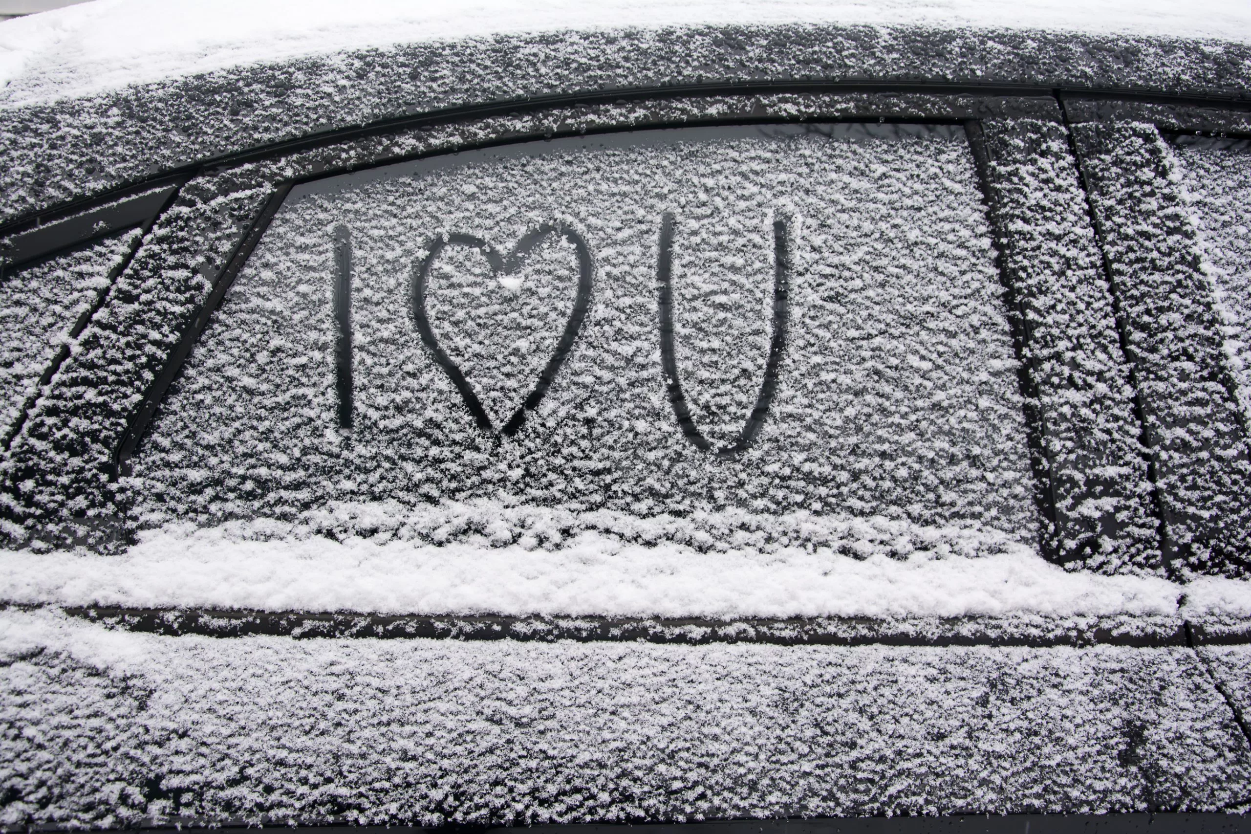 Car Window Covered in a powdery snow, the term I Heart you is drawn onto the window with heart being the actual drawing of a heart