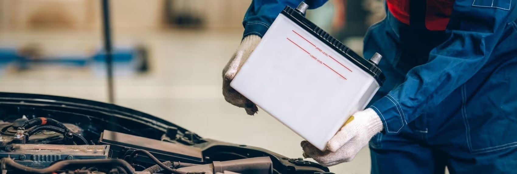 Technician lifting a new car battery into an engine bay